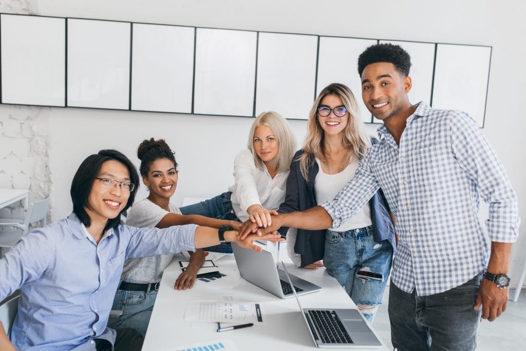 Portrait of asian young man and his african friend posing beside table with laptops and documents on it. Web-designer shaking hands with new employee in office..